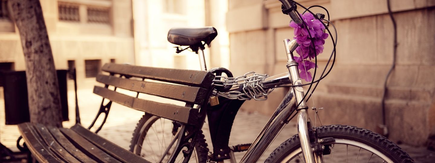 Fahrrad mit lila Blumenschmuck an eine Bank gelehnt