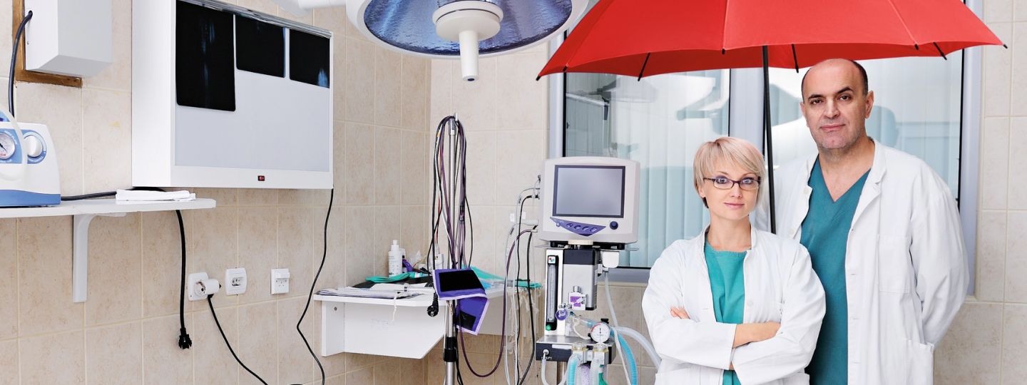 Mann und Frau aus dem Gesundheitsbereich im Behandlungszimmer unter dem roten Schutzschirm