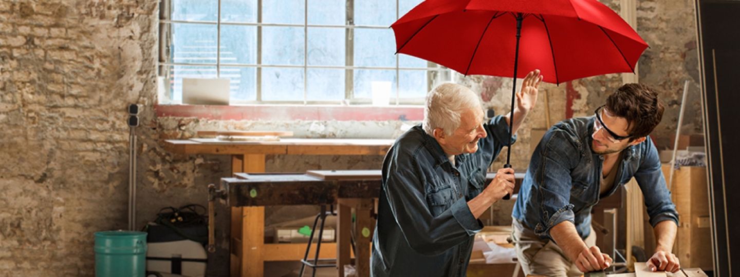 Ein jüngerer und ein älterer Handwerker sitzen unter dem roten Schutzschirm.