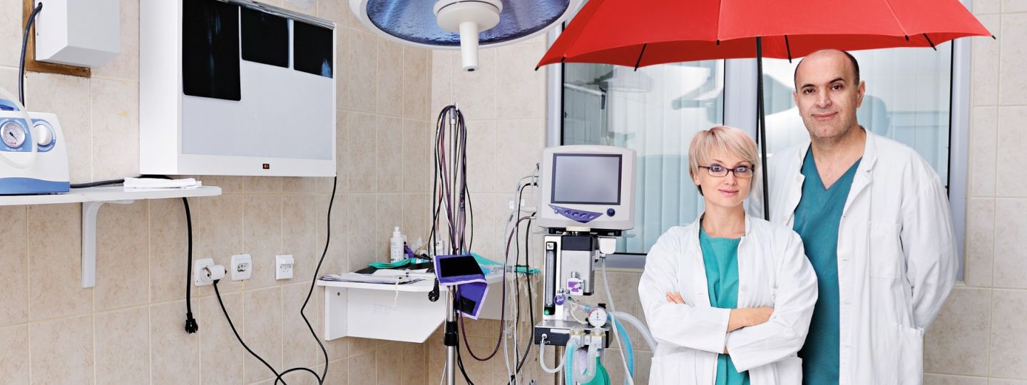 Eine Frau und ein Mann stehen mit dem roten Schutzschirm in einem Praxisraum.