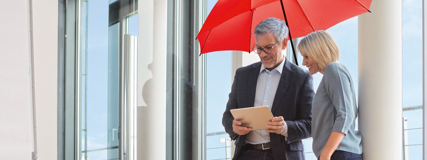 Zwei Mitarbeiter stehen unter dem roten Schirm im Büro