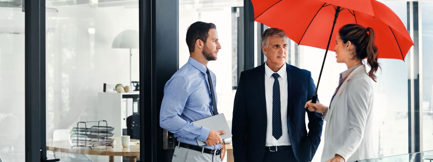 Drei Personen unterhalten sich im Büro unter dem roten Schutzschirm